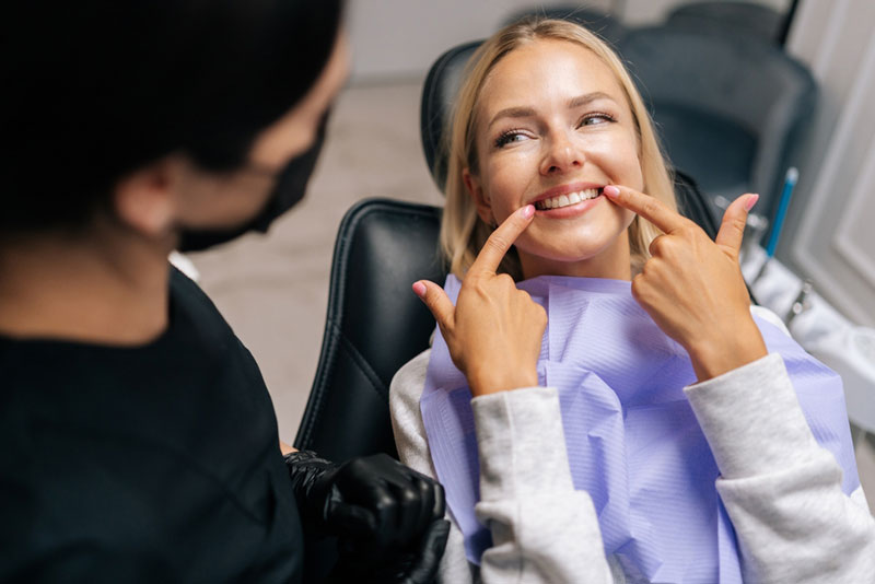 Smiling woman in dental chair pointing at her teeth after treatment, showing satisfaction with her healthy, bright smile during a dental consultation.